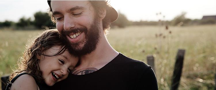 In a field, a smiling man embracing a young smiling girl.