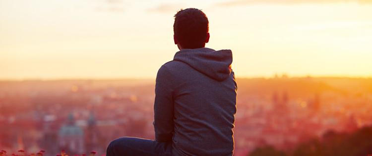 Young man turned away from camera gazing at sunset over city