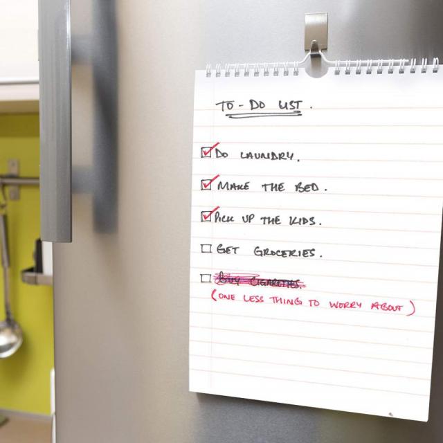 to do list hanging on a refrigerator with checked off list items saying "do laundry, make the bed, pick up the kids, get groceries" and a crossed out list item saying "buy cigarettes" with new text written underneath saying "one less thing to worry about"